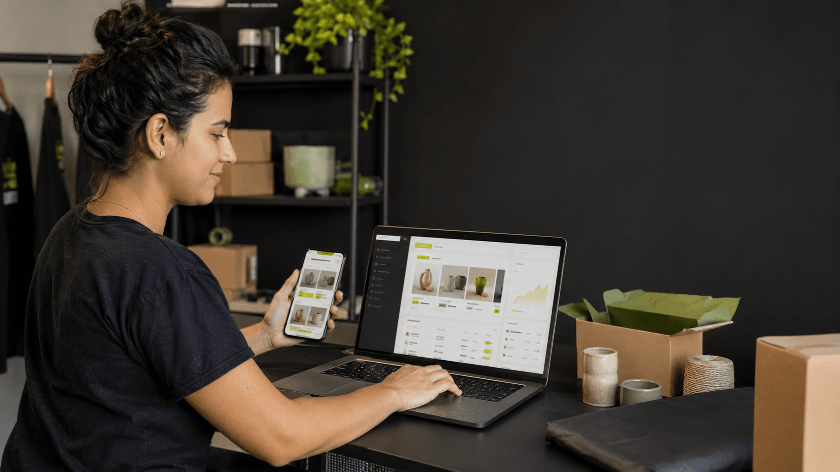Una emprendedora revisando su panel en la laptop mientras ve su tienda en el teléfono